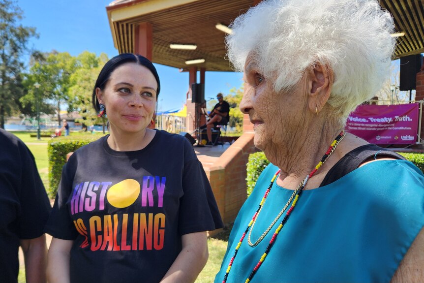 A young indigenous woman speaks with an older, white-haired elder at an outside event. 
