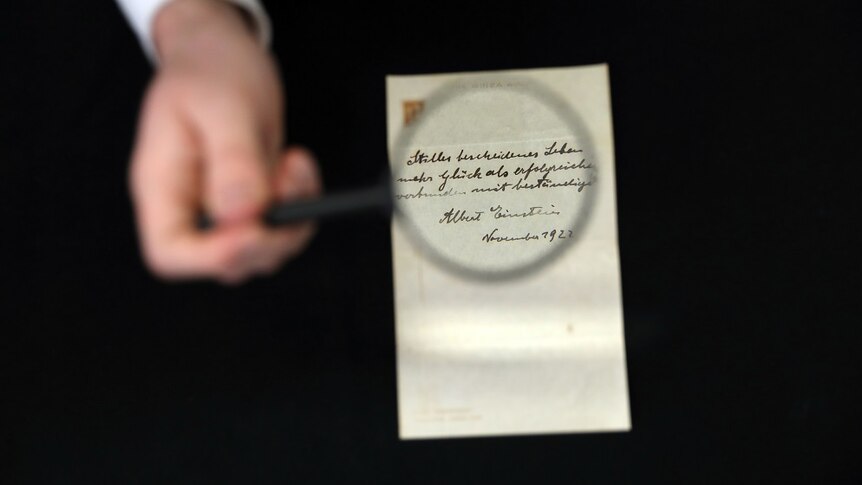 A hand holds a magnifying glass over a letter written by Albert Einstein.