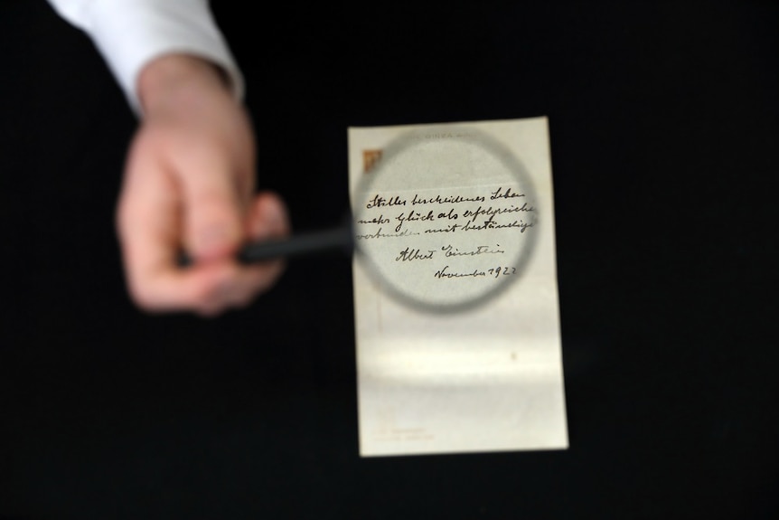 A hand holds a magnifying glass over a letter written by Albert Einstein.