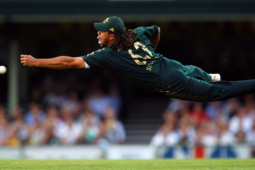 A man in cricket equipment dives to catch