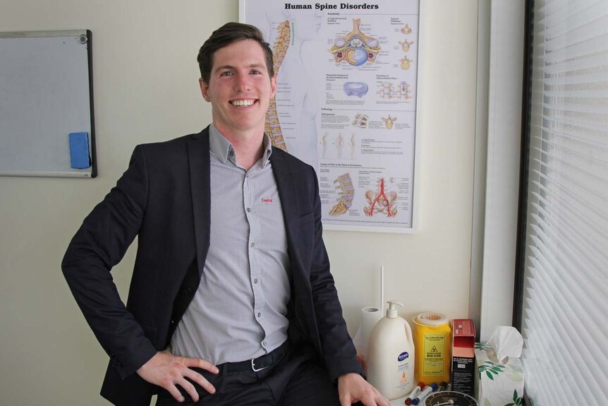 Man smiling in front of a poster with human spine disorders.