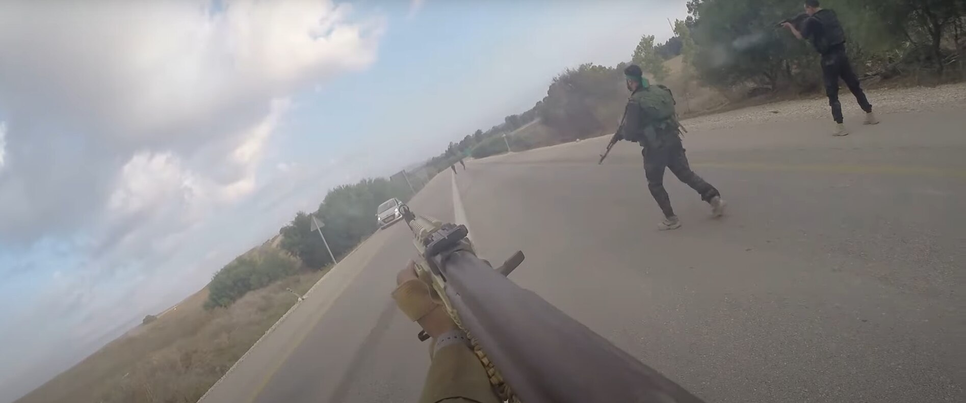 A screenshot from body camera footage showing a gun pointed down a road as a car approaches. 