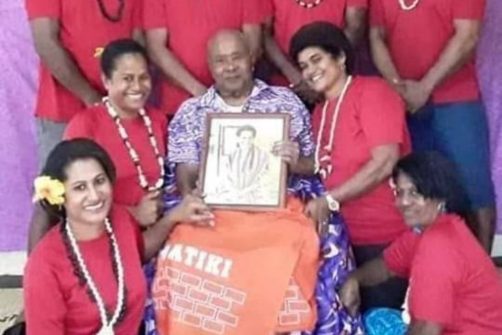 Man holds photo of woman surrounded by family.