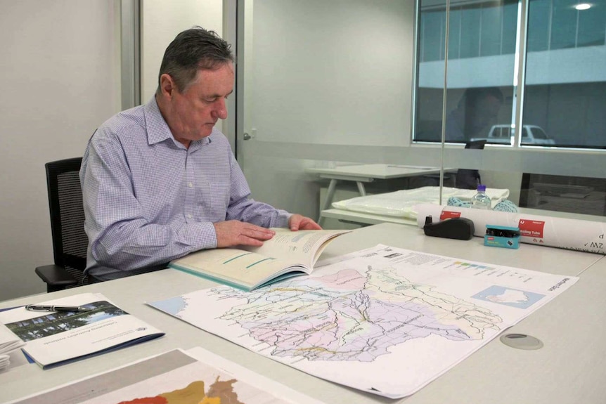 Mick Keelty sits at a desk in an office and looks at a book.