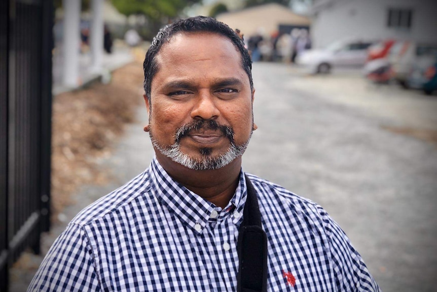 A man with a trimmed beard is wearing a buttoned up shirt