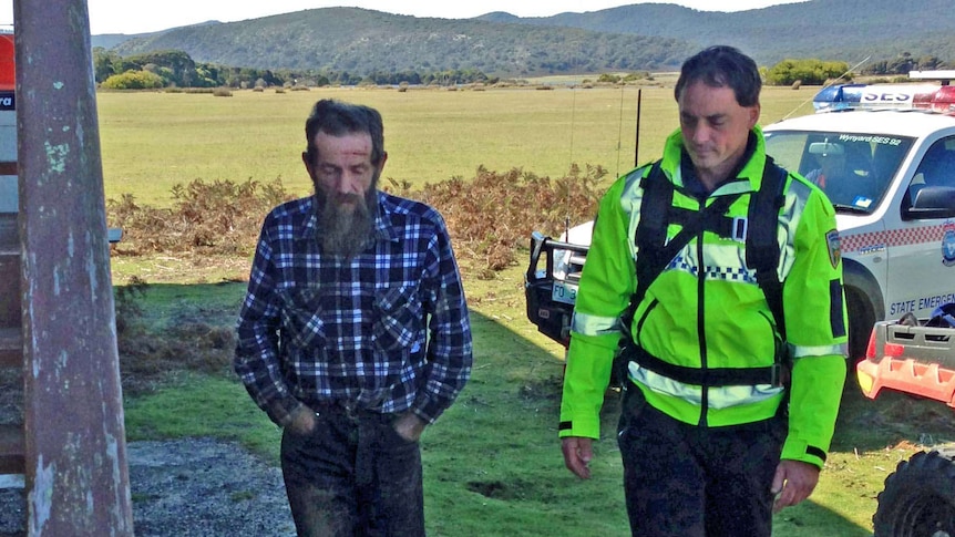 Launceston man John Norrish walks with a police officer after being found in bush in the Narawntapu National Park.