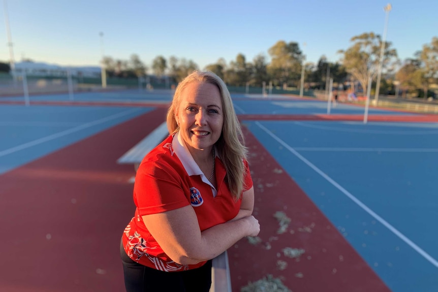 A woman in a netball shirt leans on a railing amid empty playing fields.