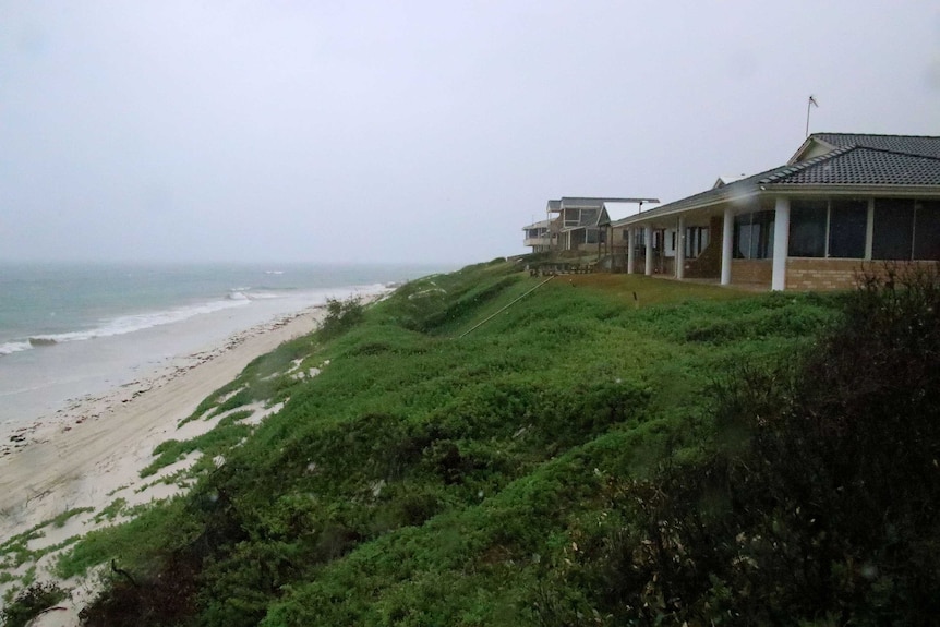 The homes sit on sand dunes covered in green low-lying plants not far from the shore.