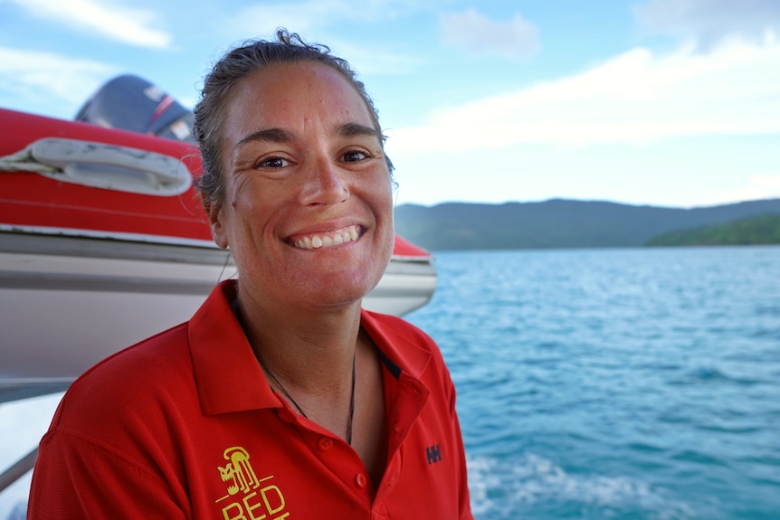 a woman in a red shirt sitting on a boat smiles at the camera