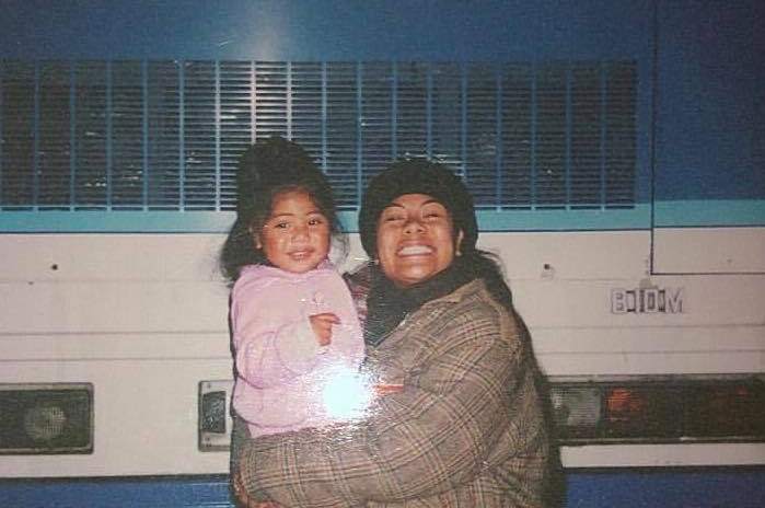 Mother holds young daughter in her arms as both smile to camera.