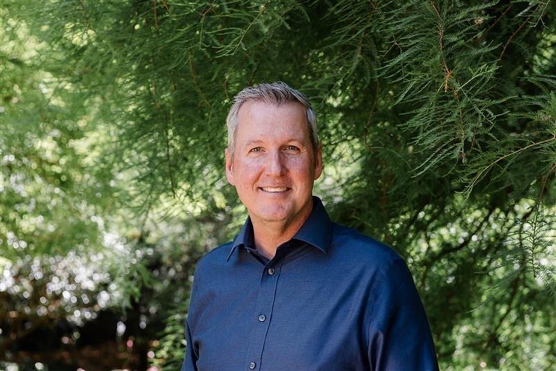 Hombre con camisa azul parada frente a los arbustos,