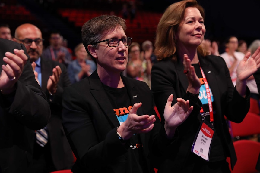Sally McManus applauds in front of a crowd