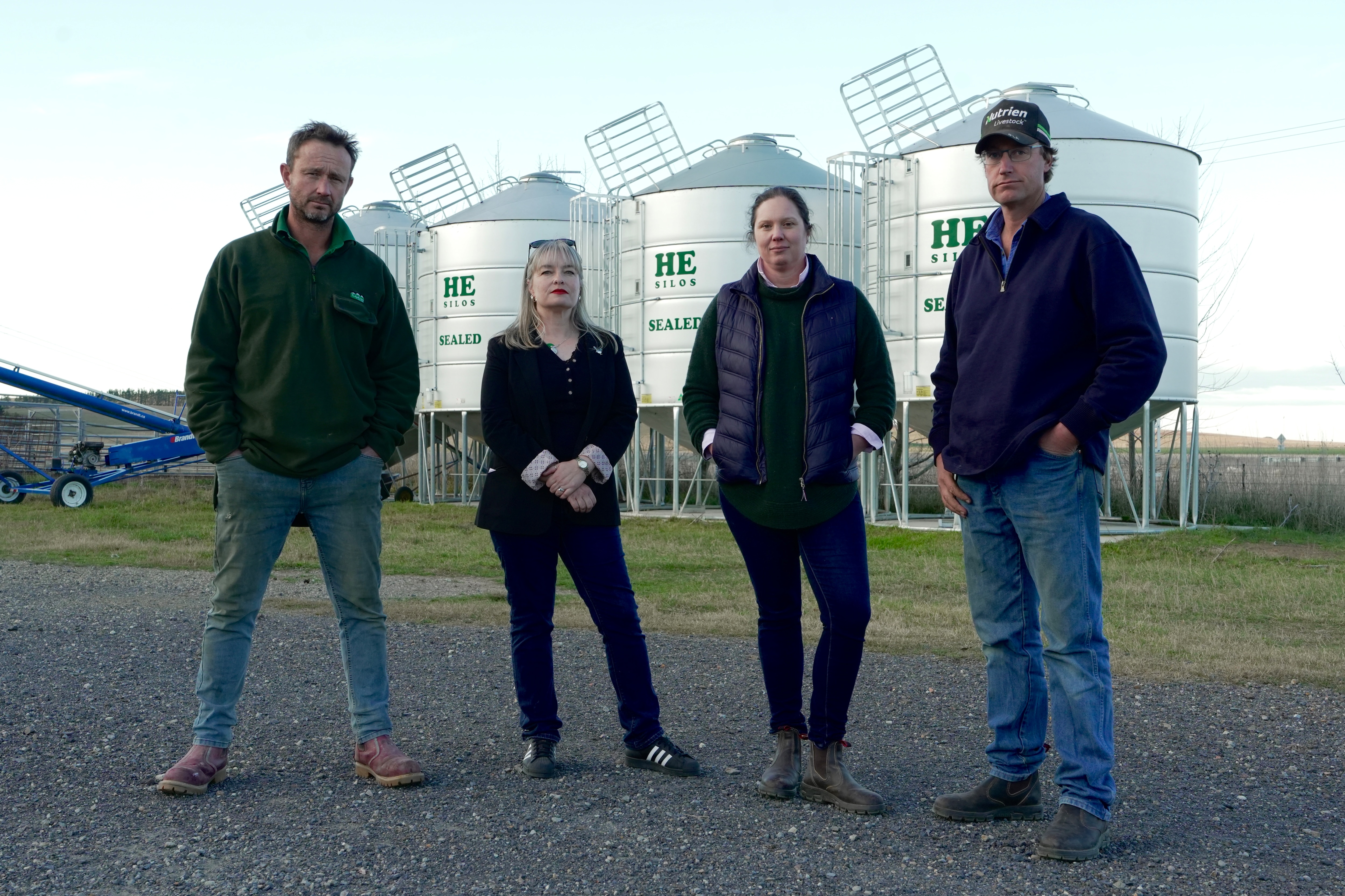 Cuatro personas, dos hombres y dos mujeres, parados frente a los silos de la granja.