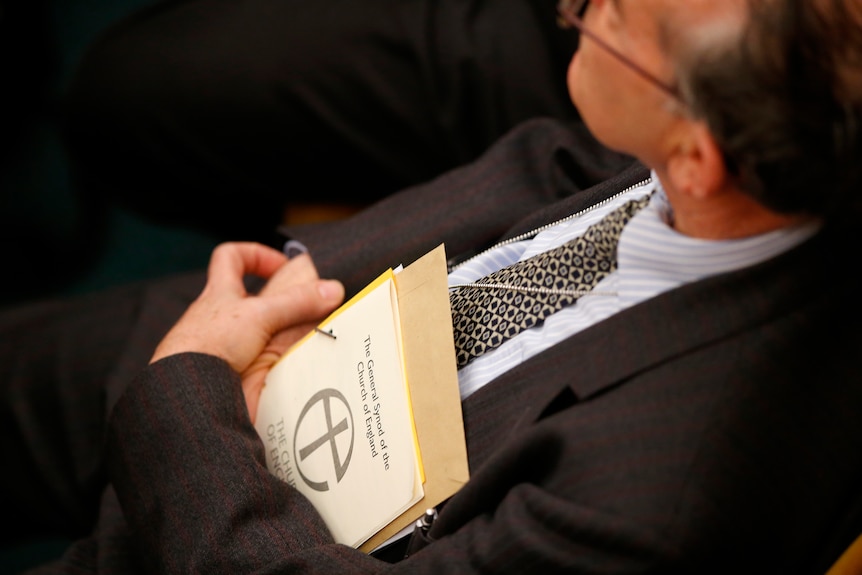 A member of the Church of England's General Synod holds a book to his chest as he listens to speeches