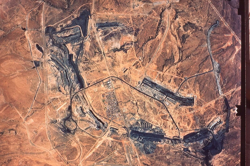 An aerial photograph of a brown landscape with a small cluster of buildings in the centre surrounded by mining operations.