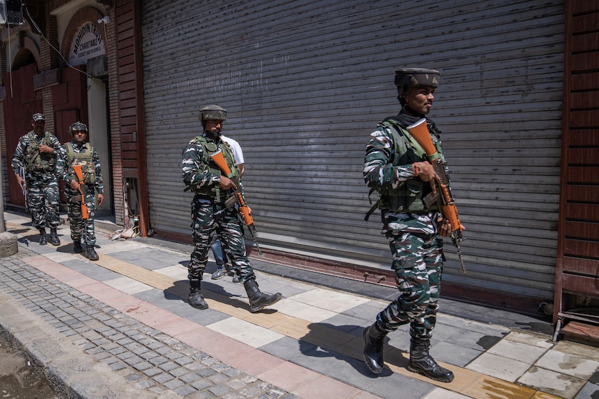 Indian paramilitary soldiers dressed in uniform patrol a street