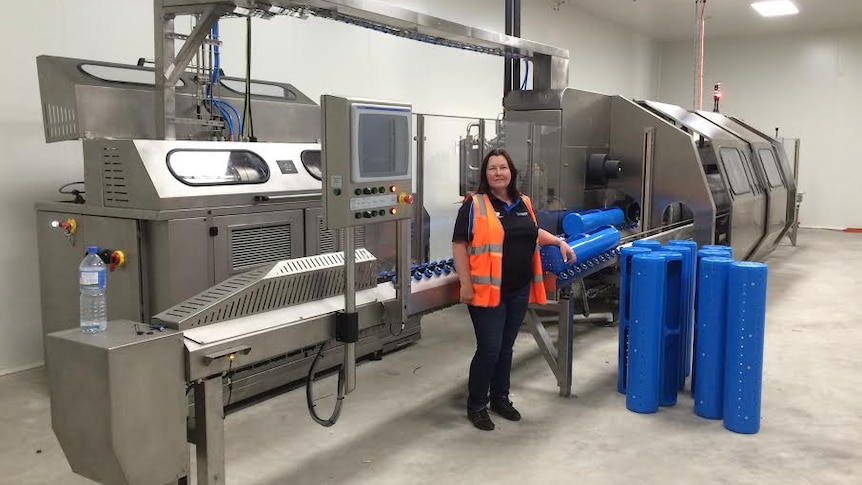 A woman stands next to a large metal food processing machine.