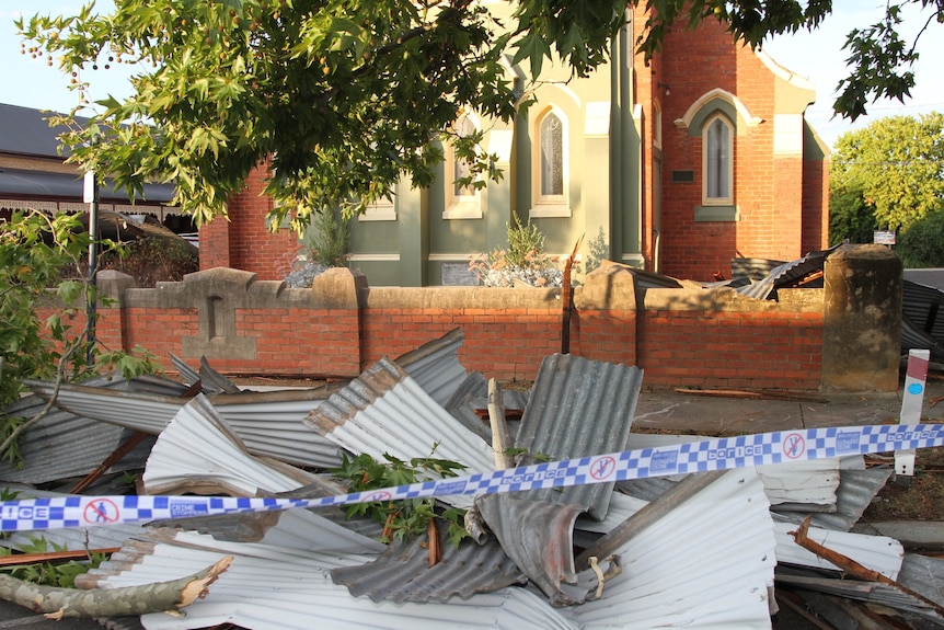 Police tape across a pile of corrugated iron in front of a damaged brick church.