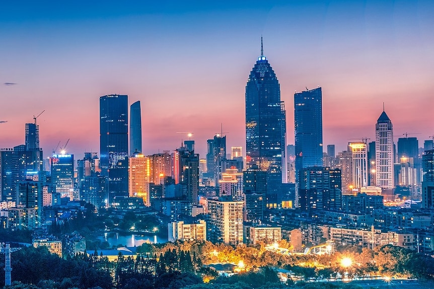 The skyline of Wuhan's Xibeihu area at dusk. There are skyscrapers and bright lights, and the sky is pink and blue.