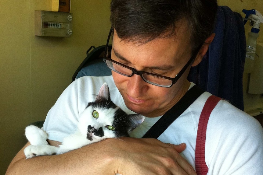 A man cuddles and fluffy black and white cat.