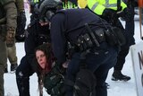  A white woman with dreadlocks kneels on the ground as police grab her.