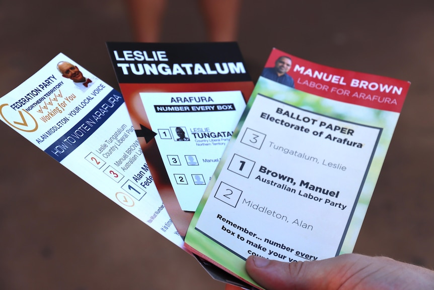 A person holds three how to vote cards for 3 different political candidates