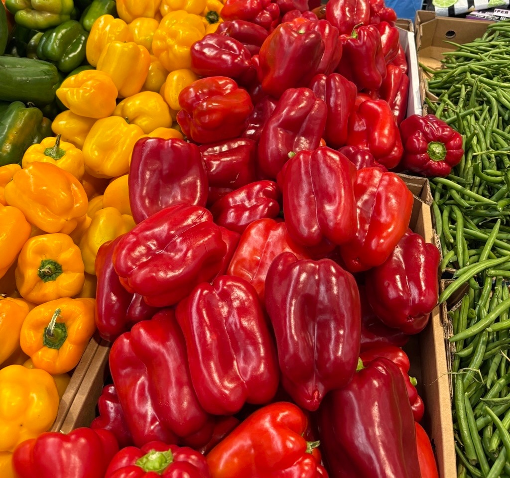 Un mercado de exhibición de pimientos amarillos, pimientos rojos y judías verdes frescos.