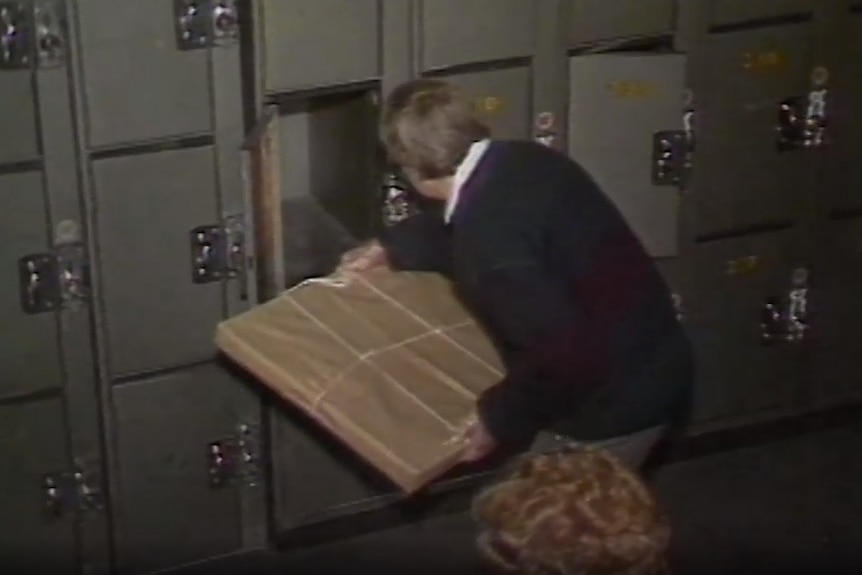 A man removes a brown parcel, containing the painting, from locker 227.