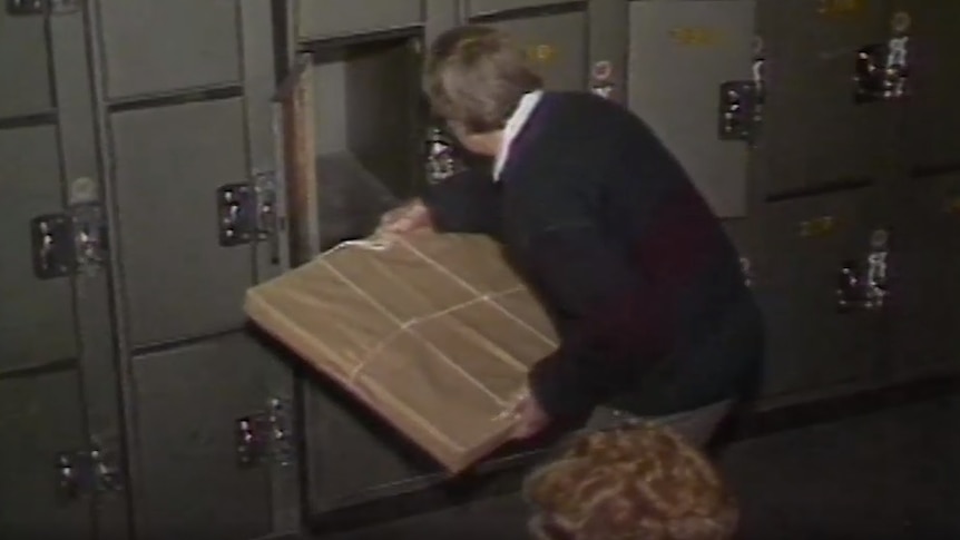 A man removes a brown parcel, containing the painting, from locker 227.