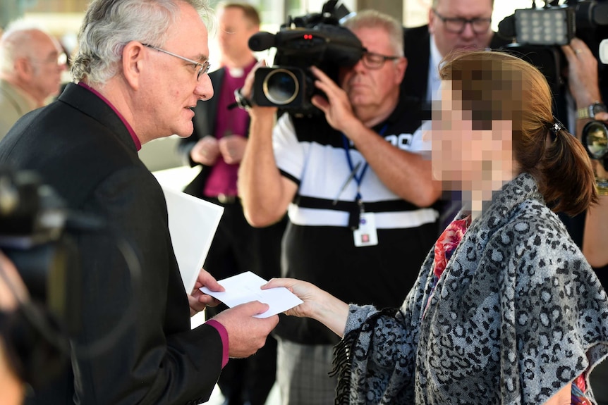 The sister of a former St Paul's student hands a letter to the Anglican Archbishop of Brisbane Phillip Aspinall