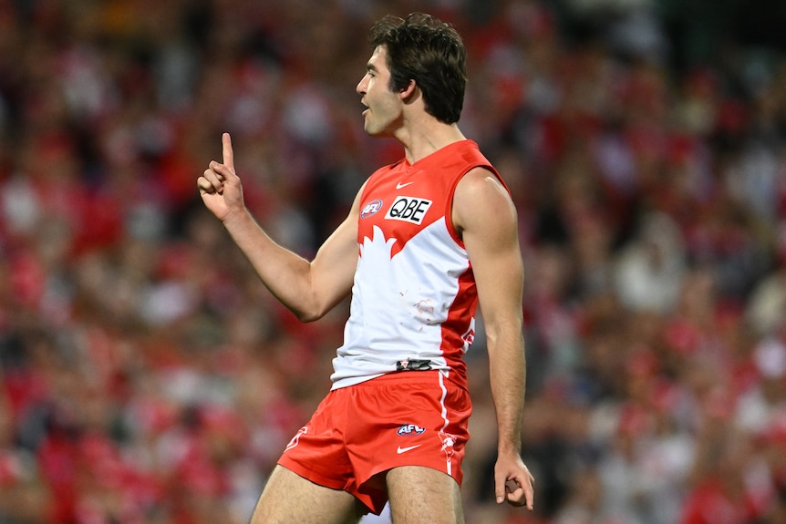 Un jugador de la AFL de los Sydney Swans señala con el dedo en su mano derecha mientras celebra un gol.