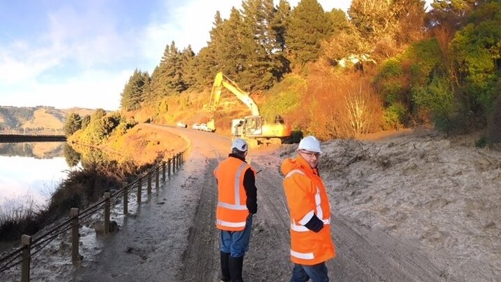 Workers in bight vests stand on mud covered State Highway 88 from Maia to Roseneath
