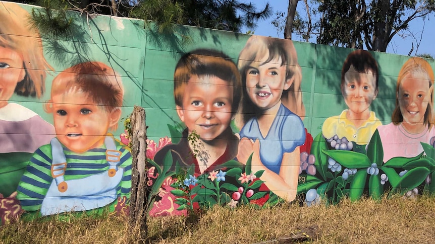 Street art of children's faces painted on a highway soundwall.