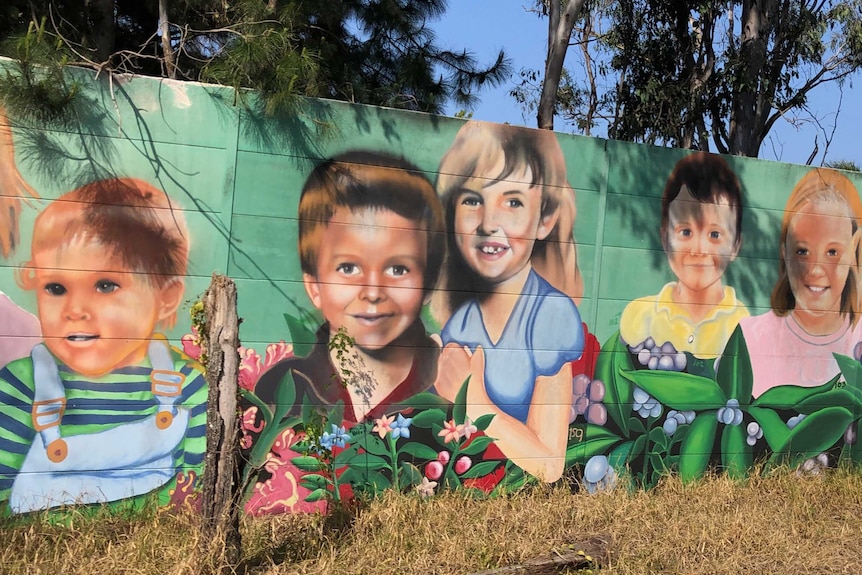 Street art of children's faces painted on a highway soundwall.