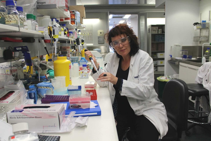 Natasha Mitchell wearing a lab coat and holding gene-editing equipment.