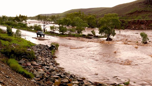 Fast flowing brown water surges down a rocky red valley in the Pilbara. The Harding River has broken its banks