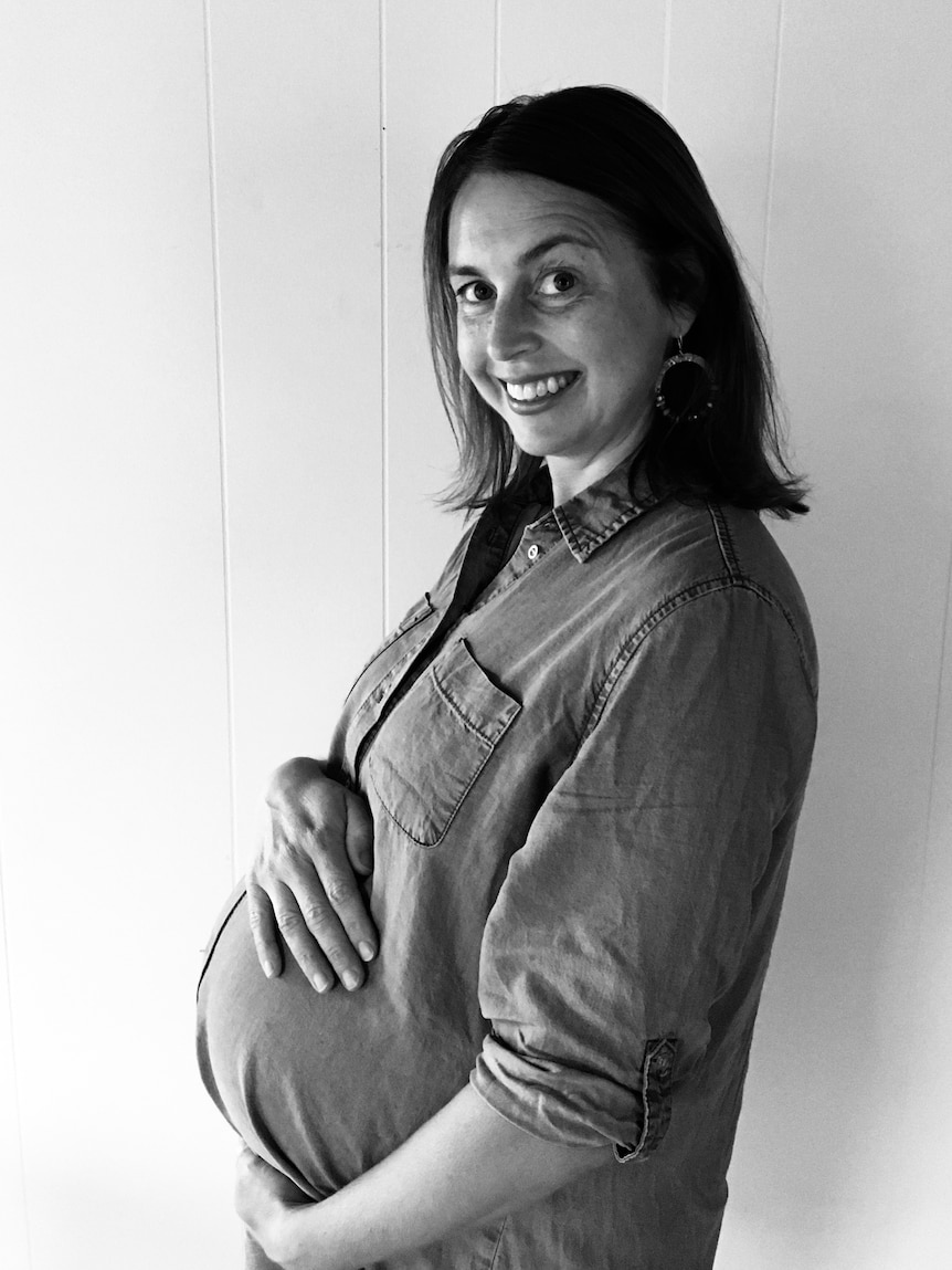 A pregnant woman smiles side on holding her belly
