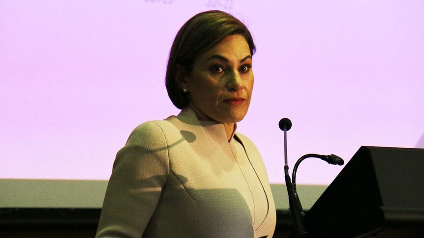 Queensland Treasurer Jackie Trad stands at a lectern in front of a large coloured screen