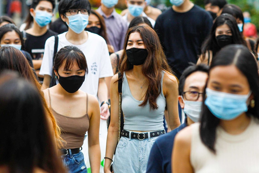 A group of people in face masks walking across a street