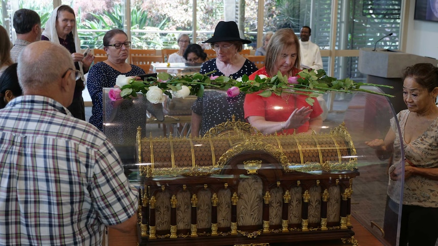 People gathered around a glass case housing an intricate reliquie box made out of wood and gold.