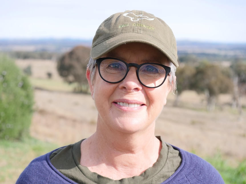 A woman wearing a cap and wearing glasses smiles at the camera