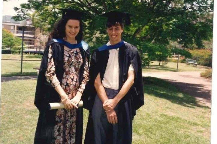 Man and woman standing on a lawn wearing academic gowns.