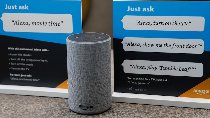 A cylindrical speaker device stands between two information placards advertising Amazon Alexa