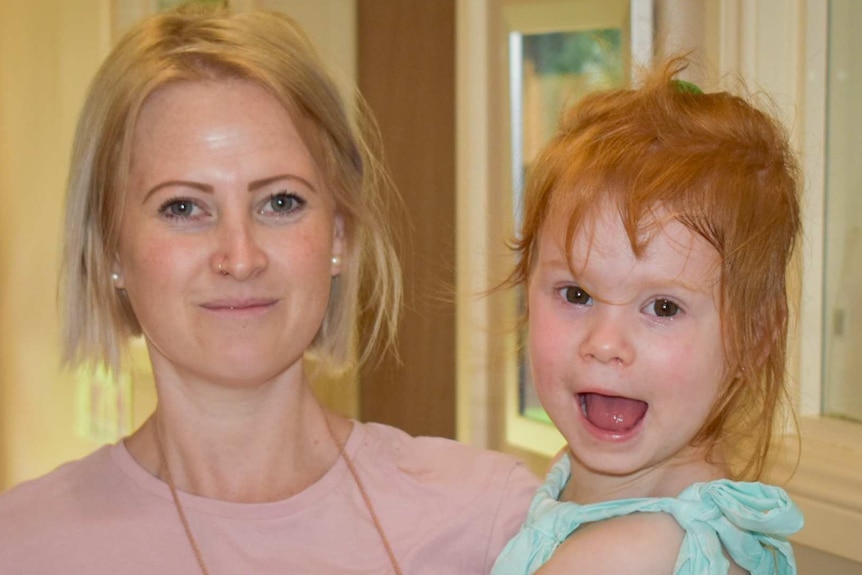 Young mum with blonde hair with child on hip, child has big smile and red hair.