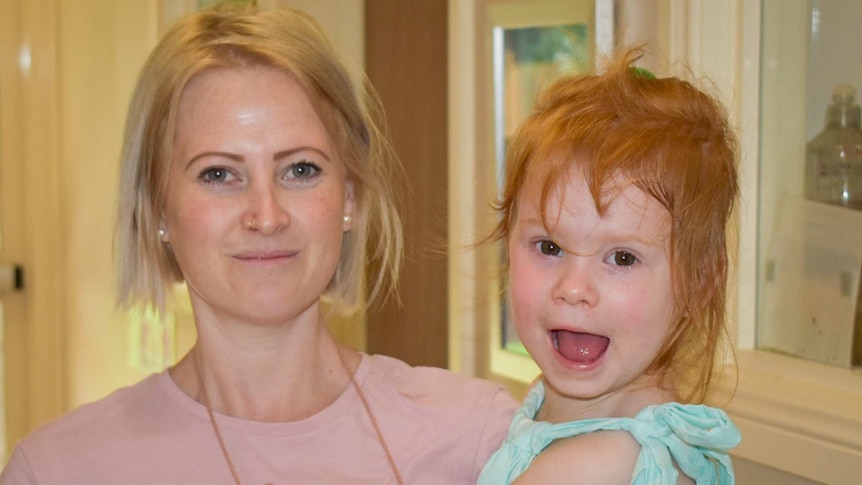 Young mum with blonde hair with child on hip, child has big smile and red hair.