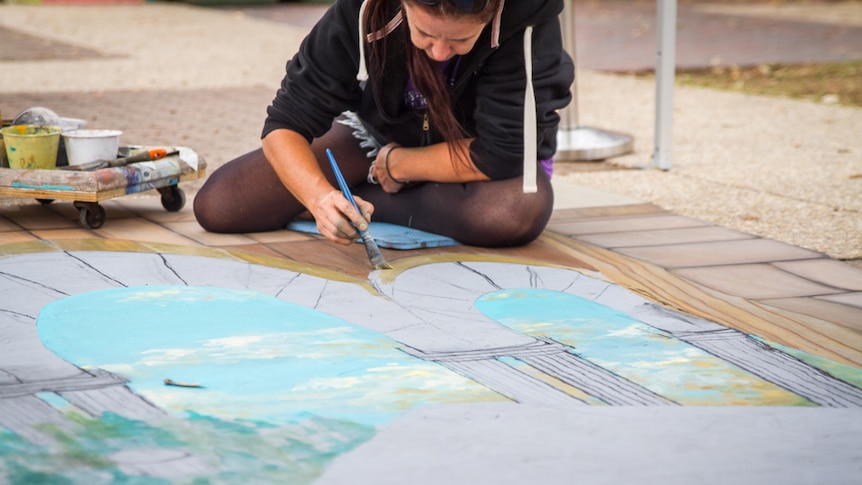 Artist Amelia Batchelor paints with chalk pigment on pavement at South Bank.