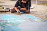 Artist Amelia Batchelor paints with chalk pigment on pavement at South Bank.