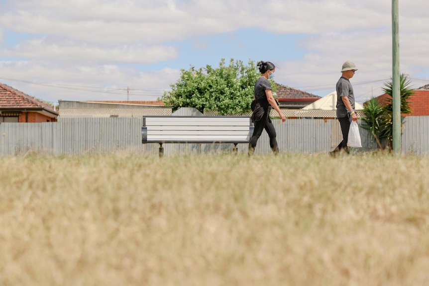 Two people walk on a footpath with no tree cover. In the foreground is long, dry grass.