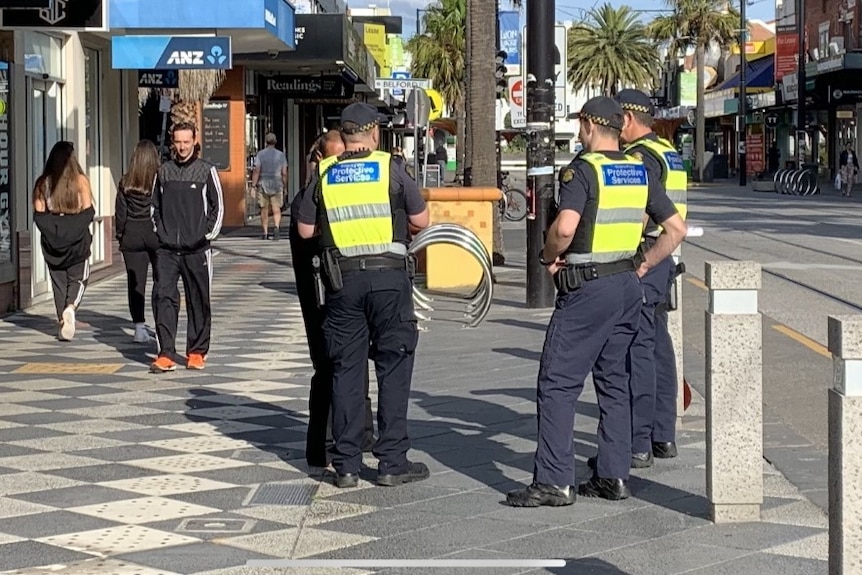 Police in high-vis tests gather around on a street in St Kilda.