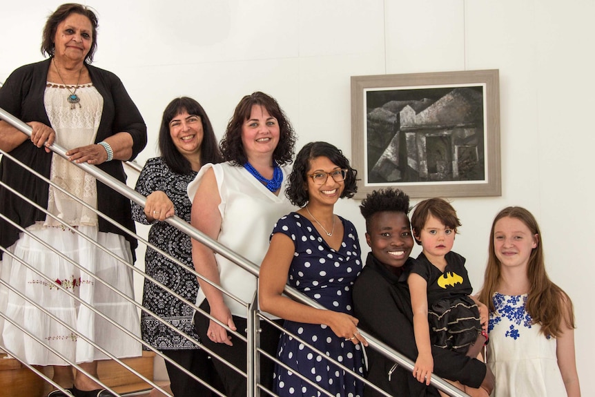 Seven women of different ages stand on a staircase.